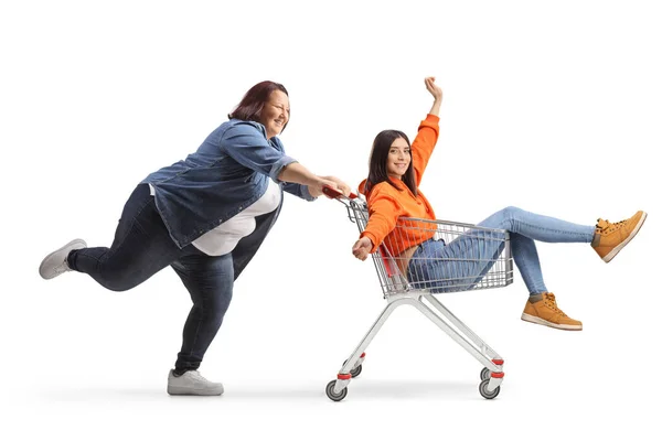 白い背景に隔離されたショッピングカート内の友人を押す太りすぎの女性の完全な長さのプロフィールショット — ストック写真