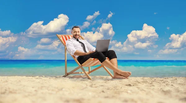 商人坐在甲板上的椅子上 在沙滩上使用笔记本电脑 — 图库照片