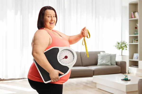 Lächelnde Übergewichtige Frau Mit Gewichtswaage Und Maßband Wohnzimmer — Stockfoto