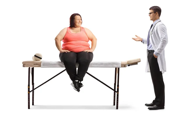 医師のアドバイスを与える太りすぎの女性に座っ上の物理的な治療ベッドの上に隔離された白い背景 — ストック写真