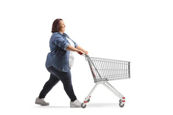 フル長さプロフィールショットのA太りすぎ女性プッシュ空ショッピングカート孤立した上の白い背景 — ストック写真