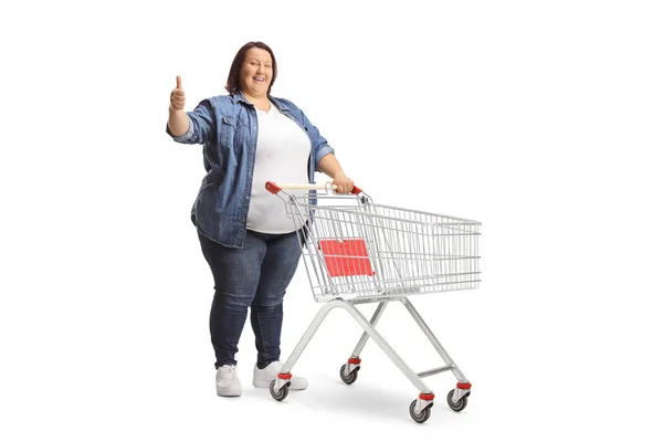 フル長いですショットの太りすぎの女性立っています空のショッピングカートとジェスチャー親指アップ隔離された白い背景 — ストック写真