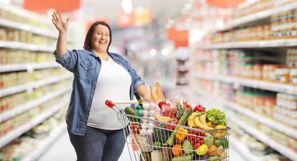 Overgewicht Vrouw Een Supermarkt Staande Met Een Winkelwagentje Zwaaiend Naar — Stockfoto