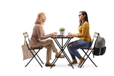 Olgun ve genç bir kadın masada oturuyor ve beyaz arka planda izole edilmiş bir fincan kahve içiyor.