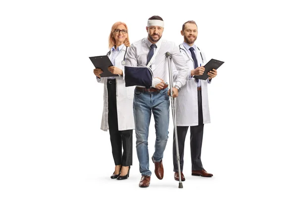 白い背景に隔離された松葉杖を持つ負傷した頭と腕の立っている医者と男のチーム — ストック写真