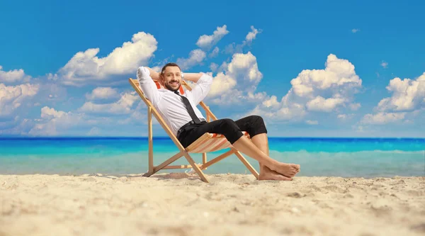 海のそばのビーチに腰を下ろしてカメラを見て笑っている男 — ストック写真