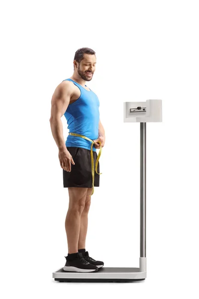 腰を測定するスポーツウェアの男の完全な長さのショットと白の背景に隔離された体重計に立って — ストック写真