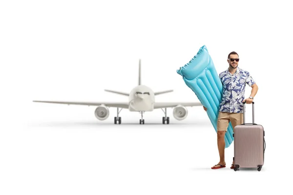 白い背景に隔離された飛行機の前にインフレータブルマットレスとスーツケースを持つ男の完全な長さの肖像画 — ストック写真