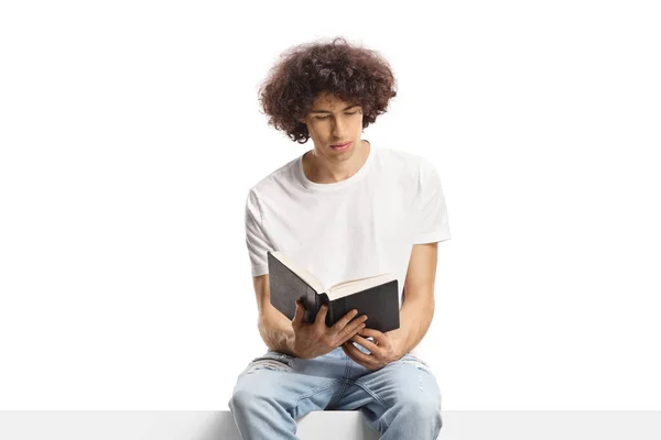 Młody Człowiek Kręconymi Włosami Siedzący Panelu Czytający Książkę Białym Tle — Zdjęcie stockowe