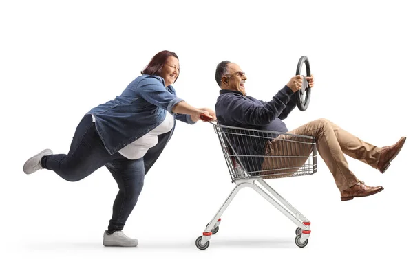 白い背景に隔離されたショッピングカートの中でハンドルを持つ成熟した男を押す女性の完全な長さプロファイルショット — ストック写真