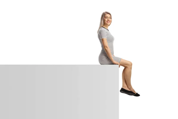 白い背景に隔離された白い壁に座っているカジュアルな若い女性 — ストック写真