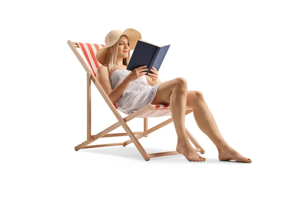 穿着白衣的年轻貌美的女人坐在沙滩上的椅子上 阅读一本以白色背景为背景的书 — 图库照片