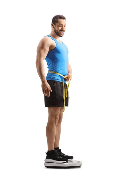 スポーツウェアを着た男が腰を測定し 白い背景に隔離された体重計に立っての完全な長さのショット — ストック写真