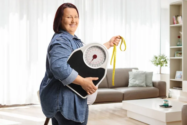 Улыбающаяся Женщина Избыточным Весом Держащая Весы Измерительную Ленту Дома — стоковое фото