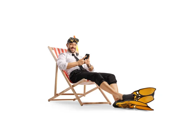商人坐在沙滩上的椅子上 戴着潜水面罩和鳍 手里拿着一个用白色背带隔开的智能手机 — 图库照片