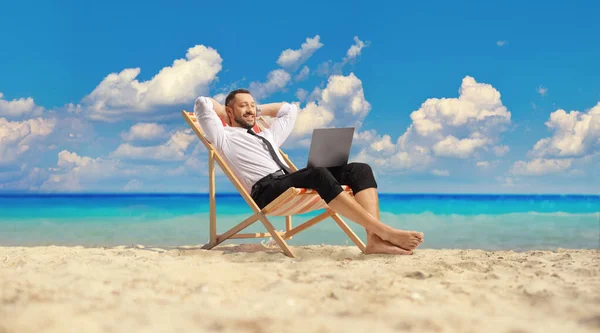 穿着衬衫和裤子的男人躺在海边 看着笔记本电脑 — 图库照片