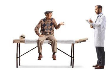 Yaşlı bir adam fizik tedavi yatağında oturuyor ve beyaz arka planda izole edilmiş bir doktorla konuşuyor.