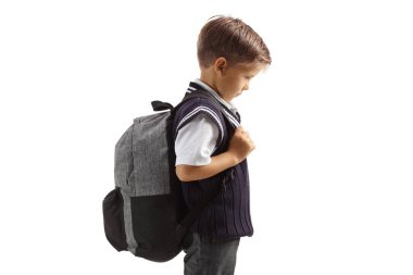 Beyaz arka planda, okul üniformalı, sırt çantalı üzgün bir çocuk.