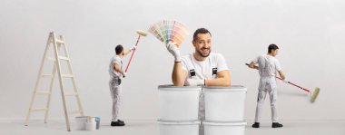 Renk paleti tutan bir ressam ve boya silindirli diğer boyacılar ve duvarı boyayan bir merdiven. 