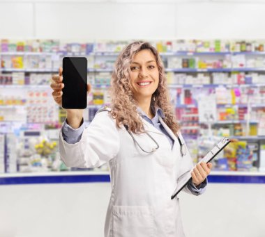 Bir eczacının elinde elinde bir doküman var. Bir eczanedeki akıllı telefonu gösteriyor.