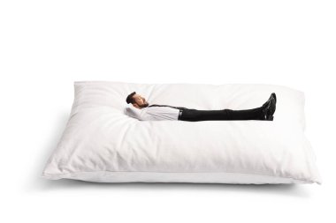 Beyaz arka planda izole edilmiş büyük bir yastığın üzerinde yatan bir iş adamı.