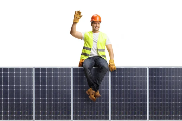 Full length portrait of a construction worker sitting on a solar panel isolated on white background
