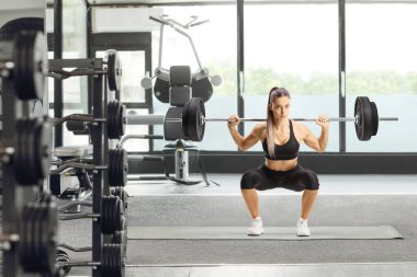 Vücut geliştiren bir kadının boy portresi ağırlık kaldırıyor ve spor salonunda diz çöküyor.