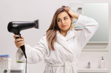 Bornozlu güzel bir kadın banyoda saçını kurutuyor.