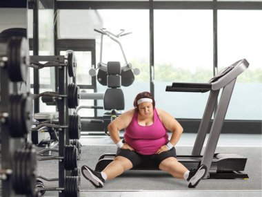Spor salonundaki koşu bandında oturan bitkin düşmüş şişman kadın.