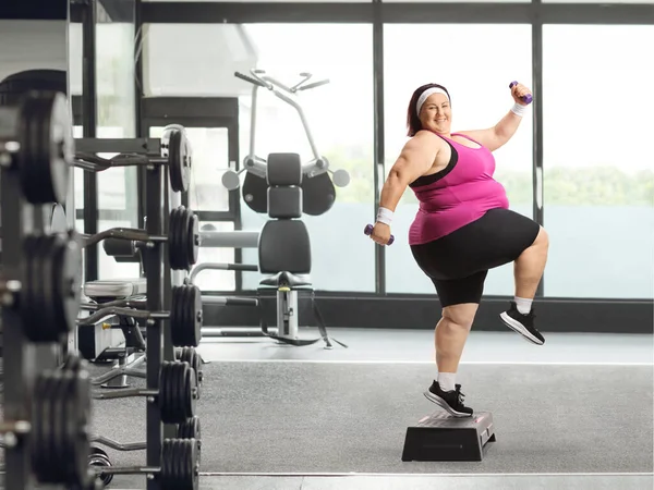 快乐而肥胖的女人在健身房进行举重和踏步运动 — 图库照片