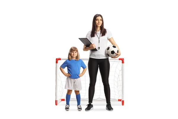 白い背景に孤立した小さな女の子とミニゴールの前に立っている女性のサッカーコーチ — ストック写真