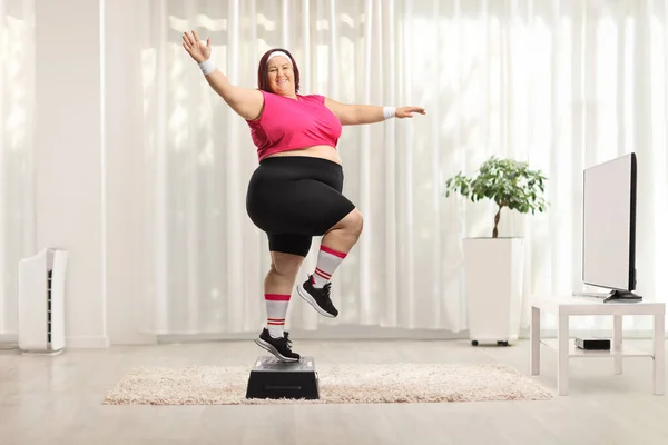 テレビの前で自宅でステップエアロビクスを行っている陽気な太りすぎの女性 — ストック写真