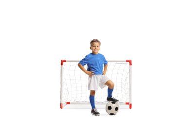 Spor formalı bir çocuk, beyaz arka planda izole edilmiş mini bir kalenin önünde futbol topuna basıyor.