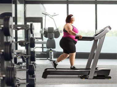 Spor salonunda koşu bandında yürüyen şişman bir kadın.