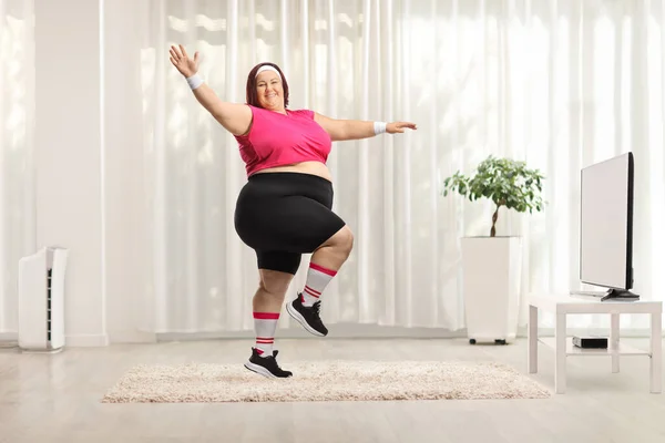 自宅でテレビの前で運動している陽気な太りすぎの若い女性 — ストック写真