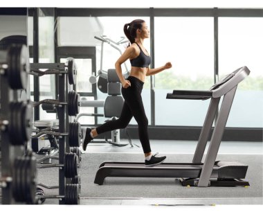 Siyah taytlı genç bir kadının spor salonunda koşu bandında koşarken tam boy profil fotoğrafı.