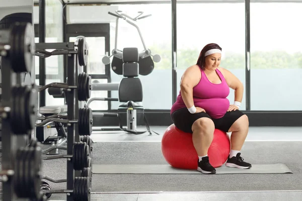 年轻而肥胖的女人坐在体育馆里的一个飞毛腿球上 — 图库照片