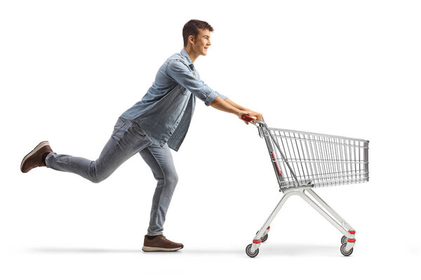 Full length profile shot of a male teenager running with an empty shopping cart isolated on white background