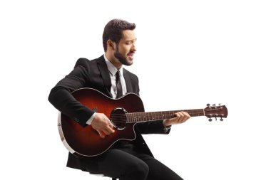 Akustik gitarlı bir müzisyen bir sandalyede oturuyor ve beyaz arka planda soyutlanmış bir şekilde çalıyor.