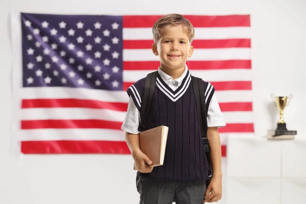 穿着校服的男孩拿着一本书 在一面美国国旗前微笑 — 图库照片