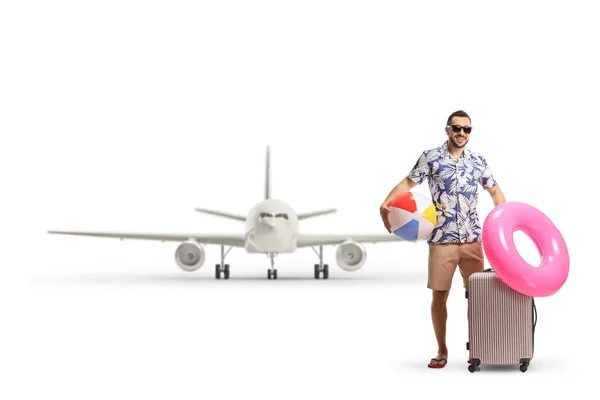 休日に旅行し 白い背景に隔離された飛行機の前でスーツケース ビーチボール 水泳リングでポーズをとる男 — ストック写真
