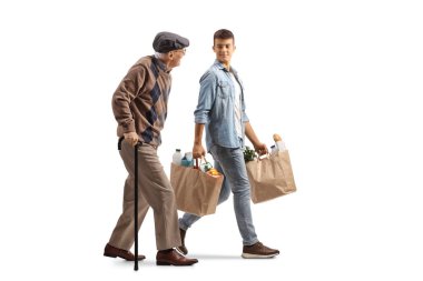 Elinde bastonla yürüyen yaşlı bir adamın ve beyaz arka planda izole edilmiş alışveriş torbalarını taşıyan kibar bir gencin tam boy profil fotoğrafı.