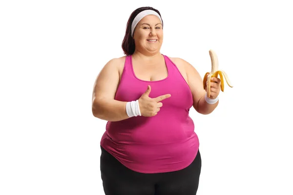 Överviktig Kvinna Sportkläder Som Håller Banan Och Pekar Isolerad Vit — Stockfoto