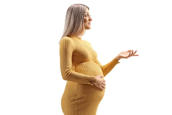 黄色いドレスの妊娠中の女性は 彼女の腹を保持し 白い背景に隔離された手でジェスチャー — ストック写真