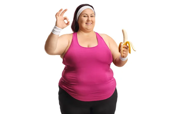 Glada Överviktiga Kvinna Sportkläder Håller Banan Och Gester Tecken Isolerad — Stockfoto
