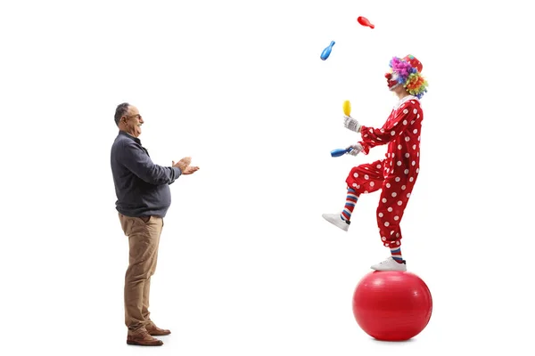 一个成熟的男人拍下了一个全长的侧面镜头 他在掌声中看着小丑在一个被白色背景隔开的球上跳着 — 图库照片