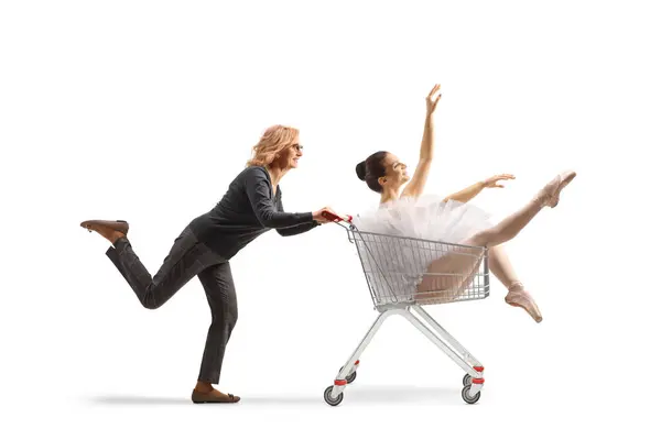 白い背景に隔離されたショッピングカートの中のバレリーナを走らせ 押す成熟した女性 — ストック写真