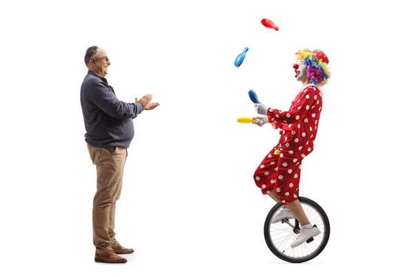 一个成熟的男人拍下了一个全长的人物形象 他给了一个骑在独轮车上的小丑掌声 还在白色背景下独自跳着杂耍 — 图库照片