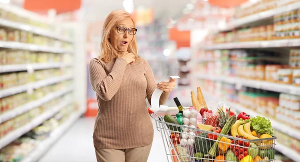 Donna Matura Con Carrello Della Spesa Che Guarda Conto Supermercato — Foto Stock