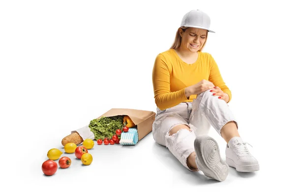Mujer Joven Con Comestibles Sentada Suelo Sosteniendo Dolorosa Rodilla Aislada — Foto de Stock